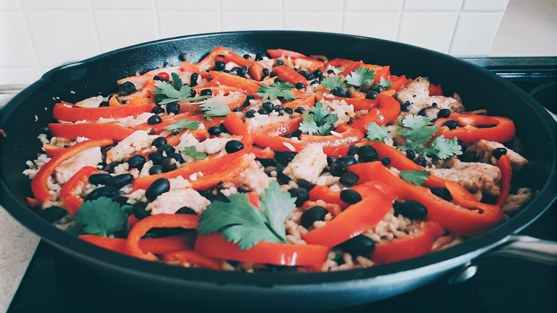 A hearty chicken, rice, and beans dish in a skillet, featuring colorful bell peppers, black beans, and cilantro. Focus keyword: chicken rice and beans recipe.